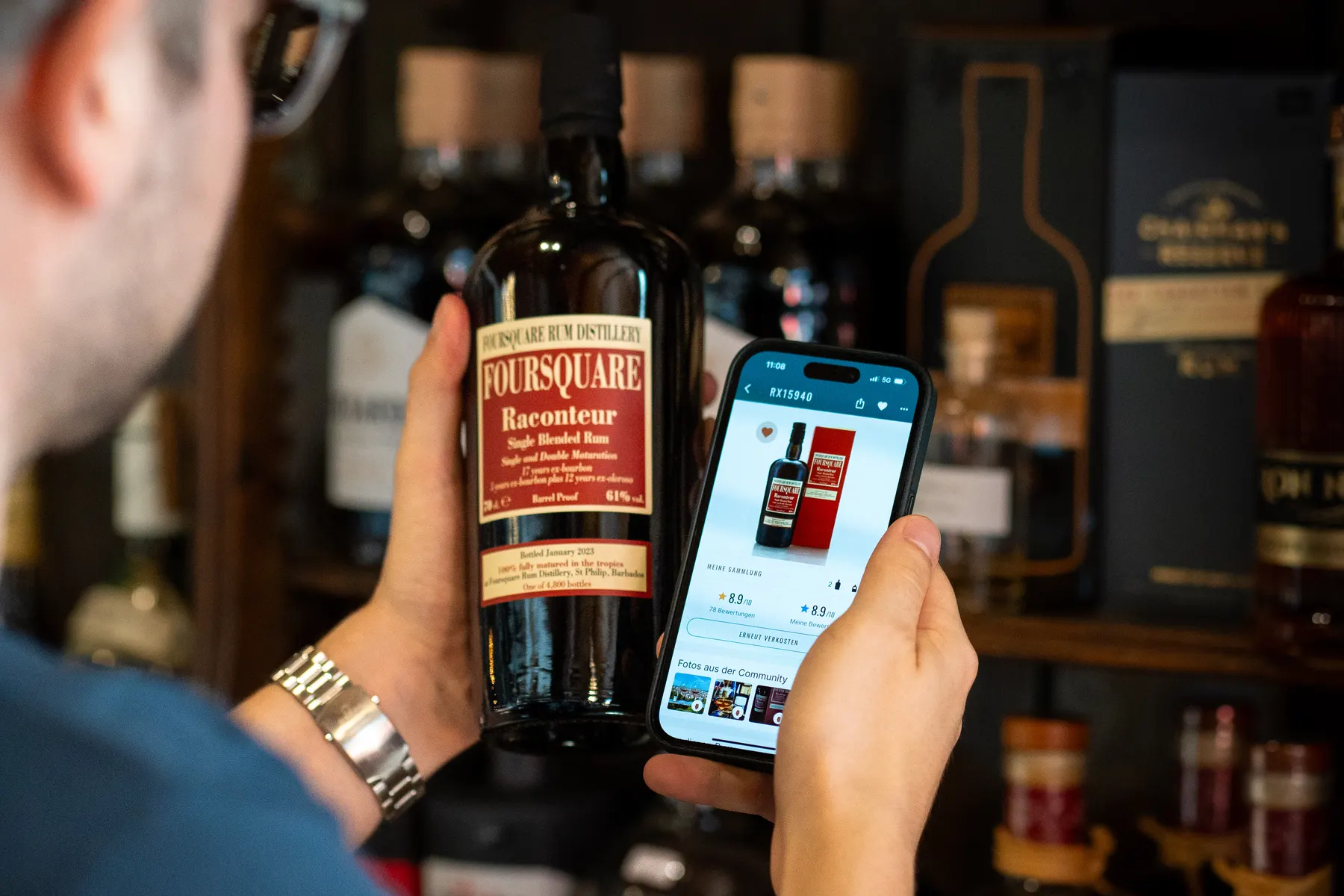 A rum lover scans a Foursquare Raconteur bottle with the RumX app, which shows the bottle's ratings and offers, in front of a full rum shelf