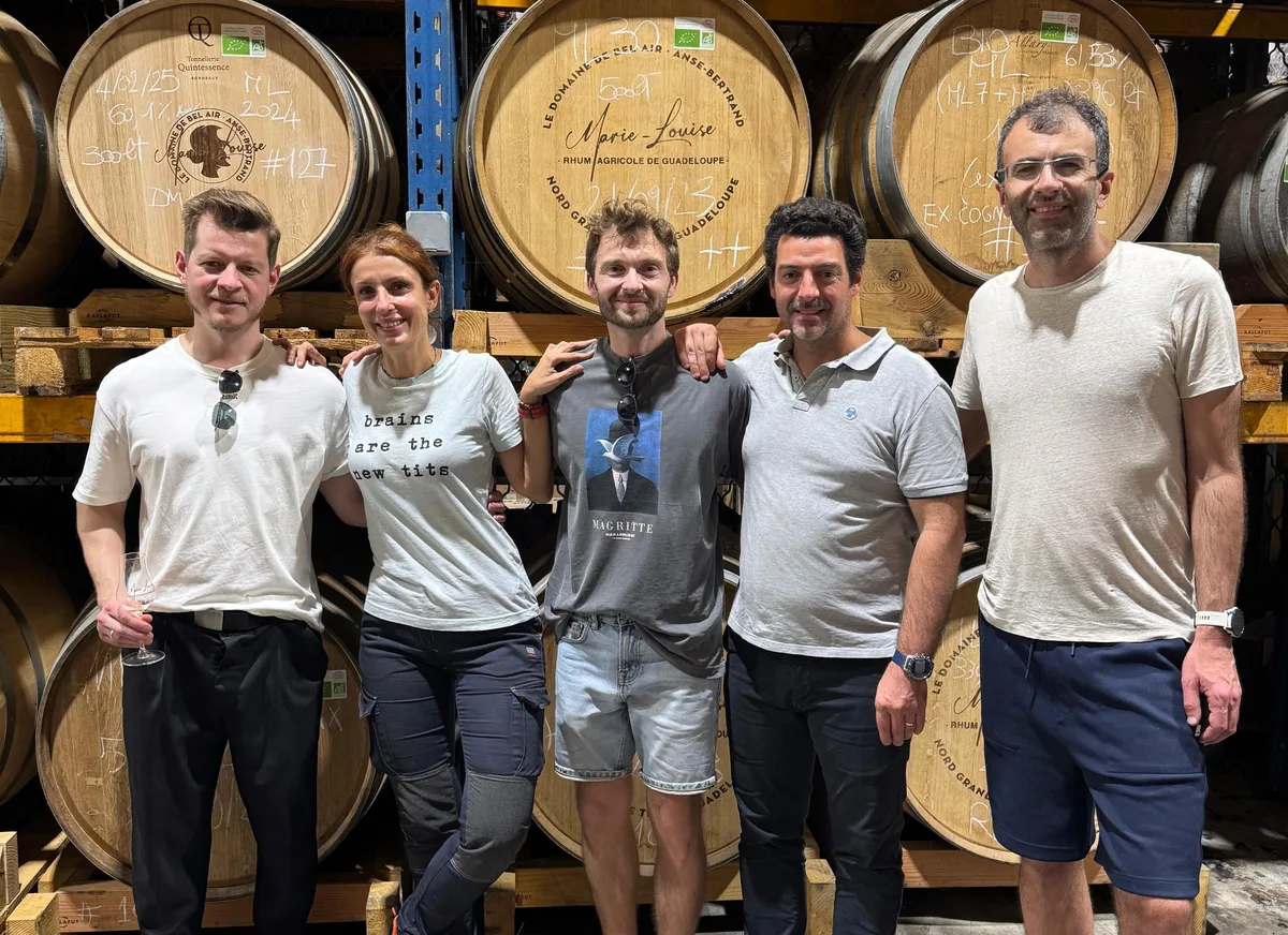 Five people standing in front of stacked rhum agricole casks in a warehouse in Guadeloupe.