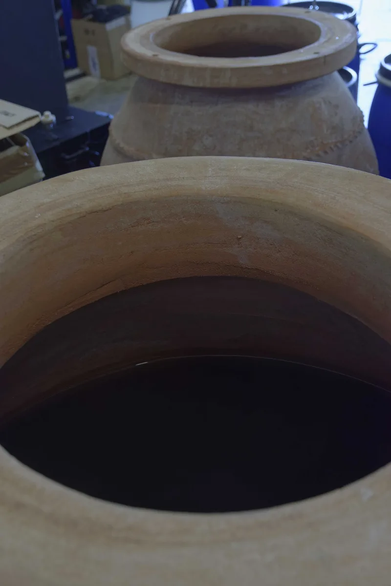Two terracotta amphorae in the cellar, the nearer one filled with dark rum.