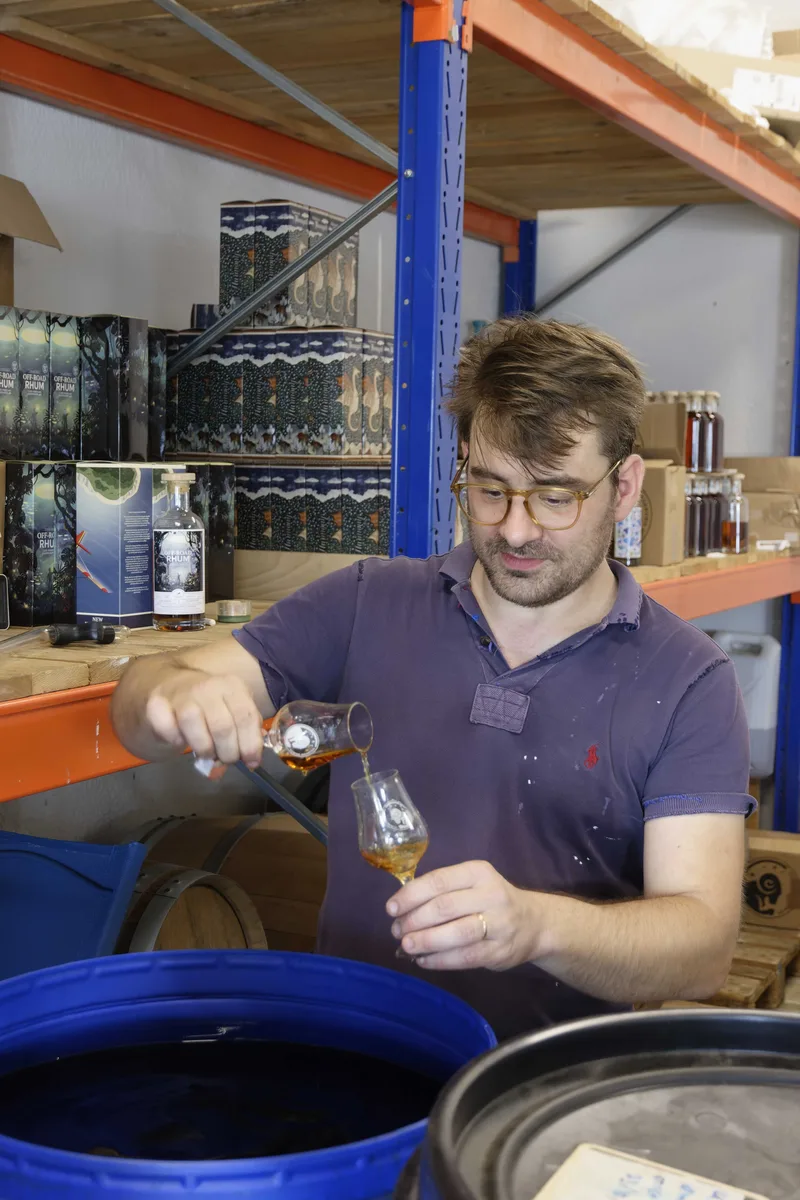 Nicolas Petit pouring a cask sample into a nosing glass, boxes of Off-Road Rhum stacked behind him.
