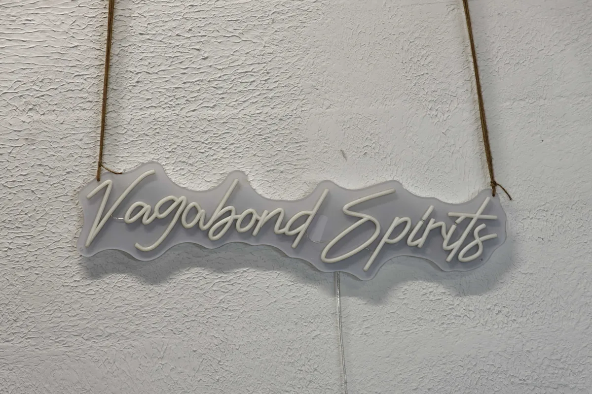 Illuminated Vagabond Spirits sign in white script, hanging from a cord on a cellar wall.