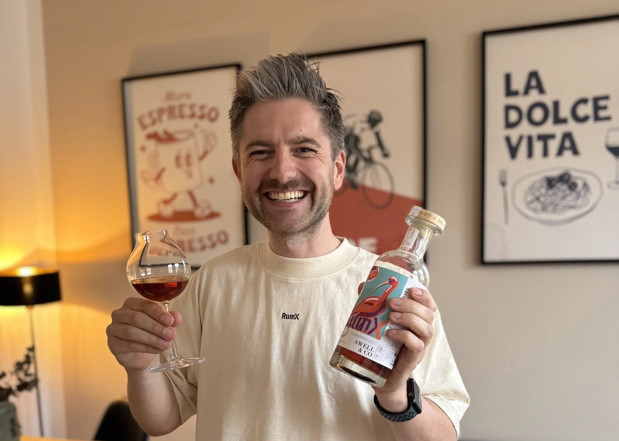 Oliver Gerhardt in a RumX shirt, smiling at the camera, holding a glass of rum and a bottle.
