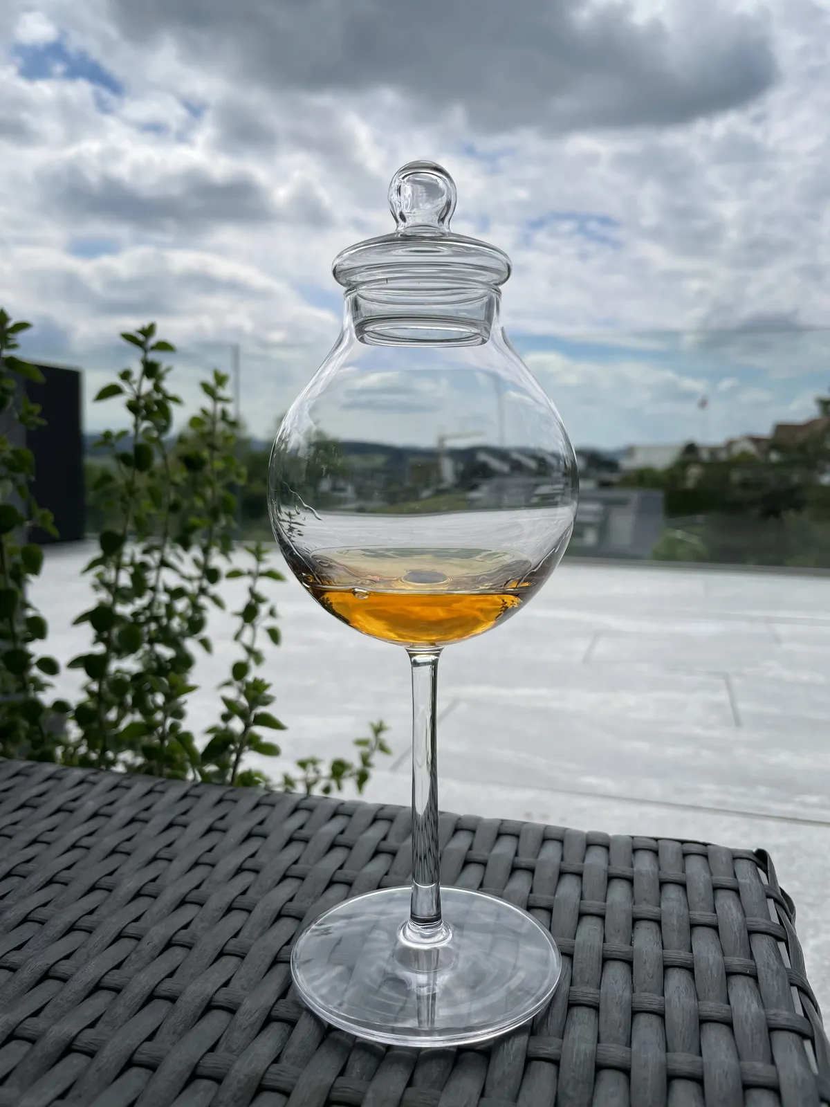 Tulip-shaped tasting glass with a button lid and a pour of rum, a terrace in the background