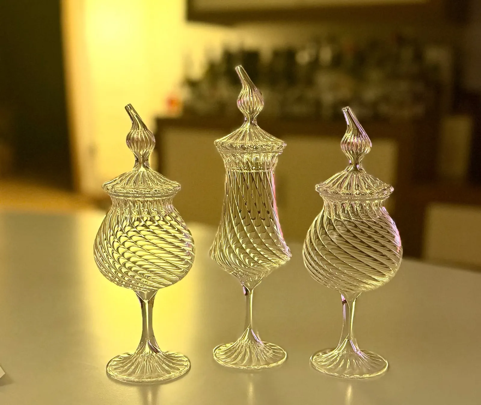 Three mouth-blown glasses with a twisted ribbed pattern and lids in warm bar light