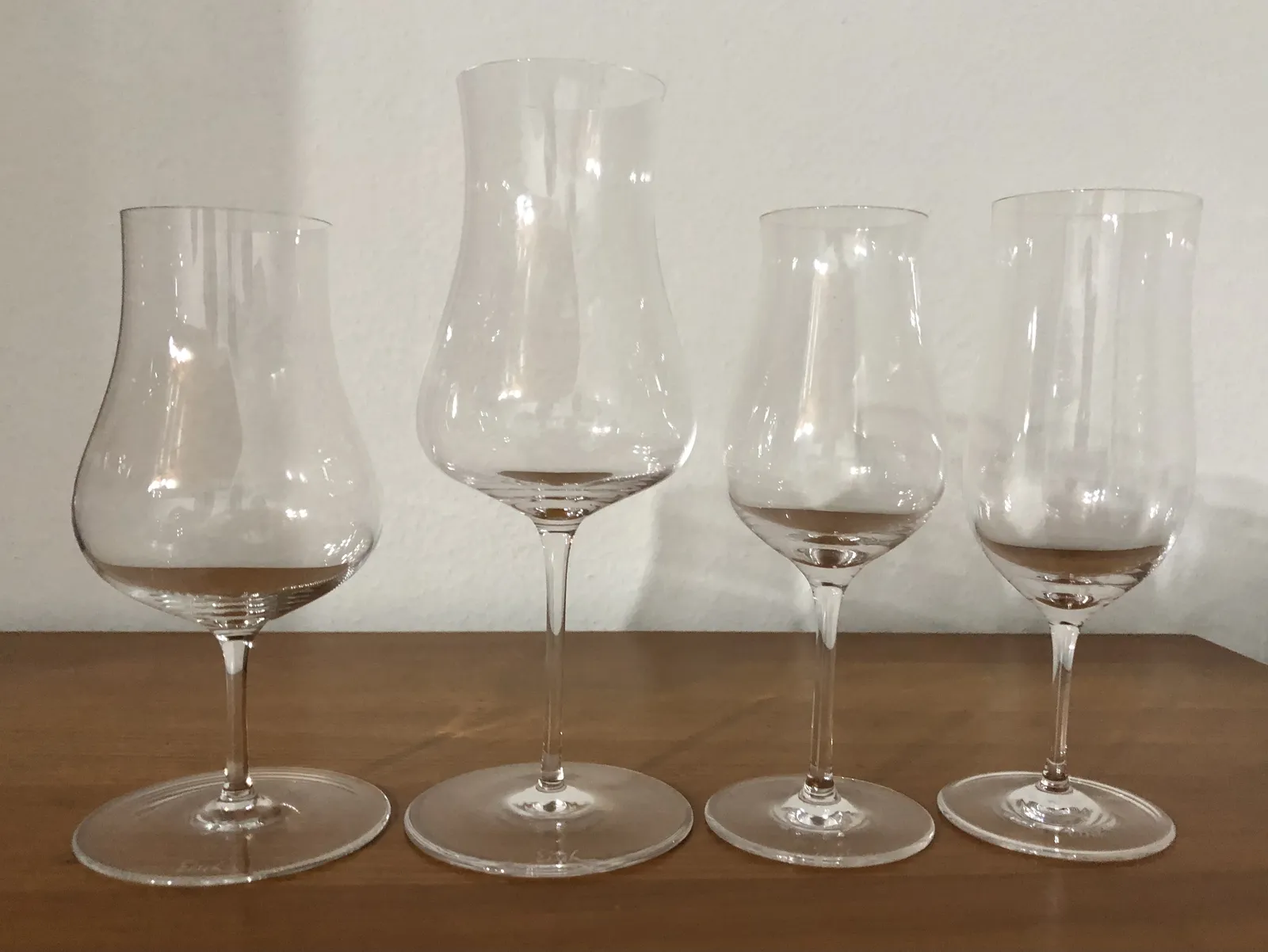 Four Eisch glasses of different shapes and sizes side by side on a wooden table