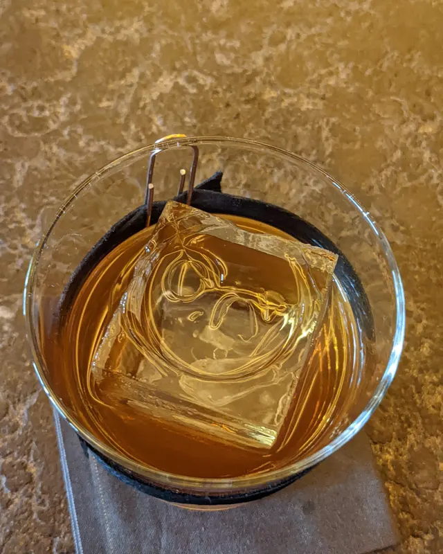 Large clear ice cube with ice tongs in a glass, photographed from above