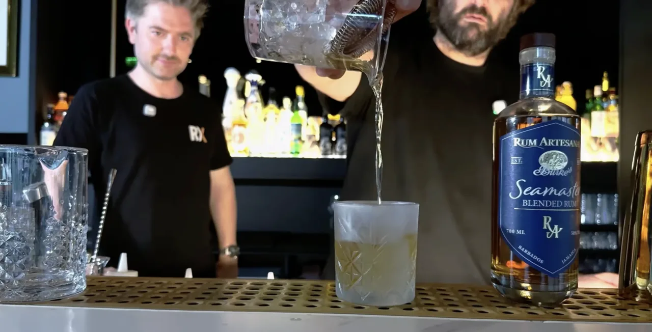 Stefan Glück strains the Seamaster Old Fashioned into a frosted tumbler, next to the bottle of Burke's Seamaster by Rum Artesanal